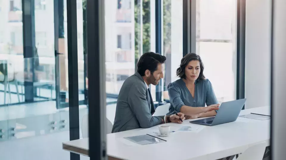 Man and women sitting at a desk and looking at a laptop